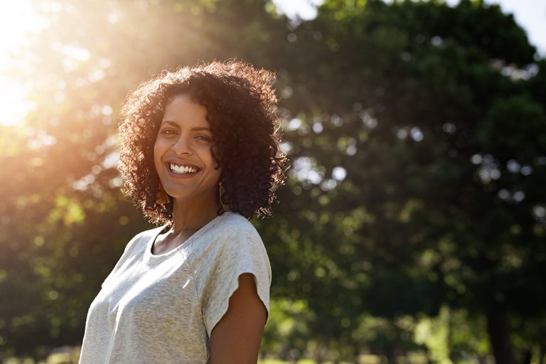 Mulher sorrindo, em pé, perto de árvores