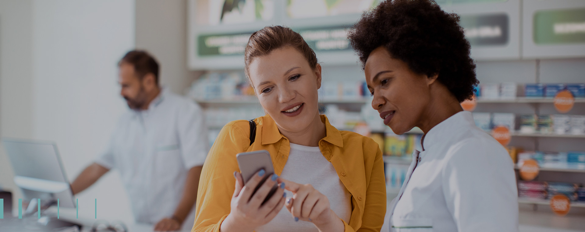 Mulher farmacêutica em pé dentro de farmácia e conversando com cliente mulher, enquanto as duas olham tela de celular