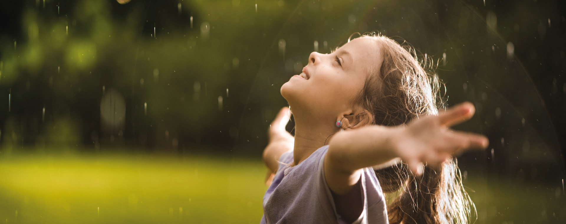 Menina sorrindo, com braços abertos, na chuva