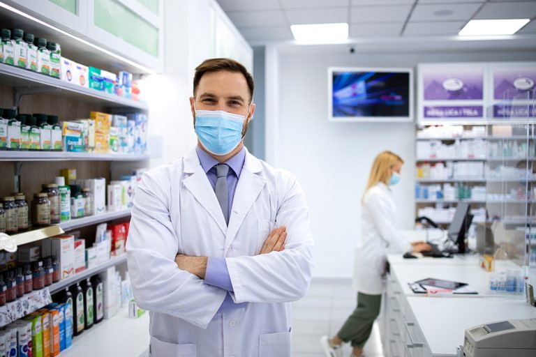 Dois farmacêuticos, em pé, dentro de uma farmácia